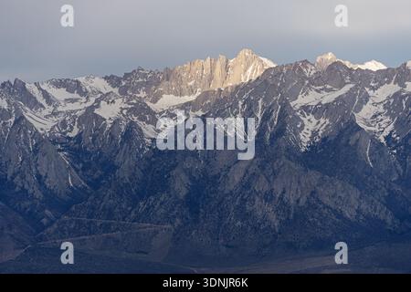 the sun breaks through the clouds and lights up the east face of Mount Whitney the highest peak in the contiguous United States Stock Photo