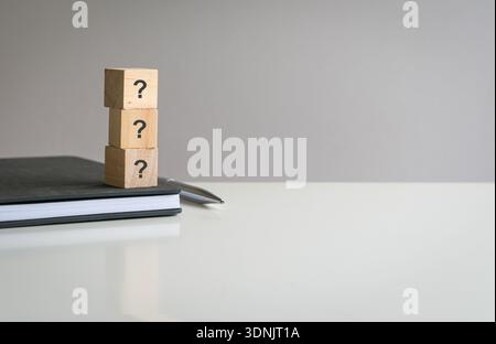Question mark on wooden blocks, in vertical order, on top of book and desk. Stock Photo