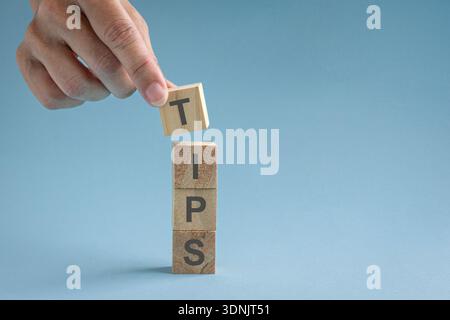 Hand stacking wood blocks for the word, Tips. Isolated on light blue surface. Stock Photo