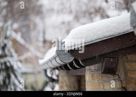 The roof is covered in white snow with snowflakes falling around. Trees are visible in the background showing the winter scene. Stock Photo