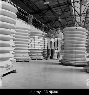Slaviansk, Ukrainian SSR, 1960s. An archive photo of two engineers reviewing technical blueprints amidst rows of massive high-voltage ceramic insulators at the Slaviansk ZVI plant. The image highlights the scale of industrial production and quality control at this major Soviet factory in the Donetsk region. Large-scale electrical porcelain products fill the workshop, illustrating the peak of the Soviet energy industry's power. A classic example of industrial heritage, technical expertise, and the peaceful Donbas economic era. Stock Photo