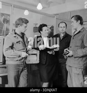 Slaviansk, Ukrainian SSR, 1960s. An archive photo of a group of engineers discussing technical data at the Slaviansk ZVI plant. A female laboratory head in a formal suit holds a reference book, surrounded by three young specialists in a professional environment. The scene, featuring industrial measuring instruments and a space-themed poster in the background, reflects the scientific progress and gender equality in Soviet engineering. A classic example of the intellectual atmosphere and human potential of the peaceful Donbas during the mid-20th century. Stock Photo