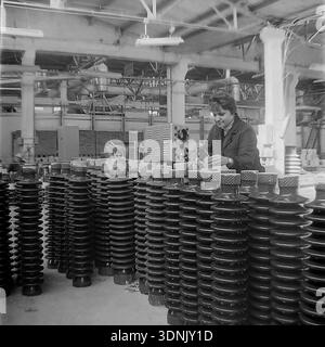 Slaviansk, Donetsk region, Ukrainian SSR, USSR. 1960s. A young female quality control technician uses a portable electronic testing device with an oscilloscope screen to inspect rows of dark glossy ceramic insulators at the High-Voltage Insulator Factory (ZVI). She carefully applies a probe to the porcelain surface. The archive series highlights the advanced technical standards, laboratory testing, and the role of women in Soviet engineering. A nostalgic view of the stable industrial routine in the peaceful Donbas before the war. Stock Photo