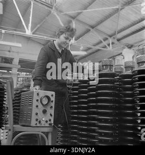 Slaviansk, Donetsk region, Ukrainian SSR, USSR. 1960s. A young female quality control technician uses a portable electronic testing device with an oscilloscope screen to inspect rows of dark glossy ceramic insulators at the High-Voltage Insulator Factory (ZVI). She carefully applies a probe to the porcelain surface. The archive series highlights the advanced technical standards, laboratory testing, and the role of women in Soviet engineering. A nostalgic view of the stable industrial routine in the peaceful Donbas before the war. Stock Photo