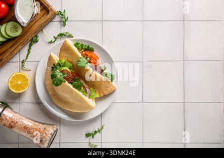 Plate of delicious pitas with falafel and fresh vegetables on white tile background Stock Photo