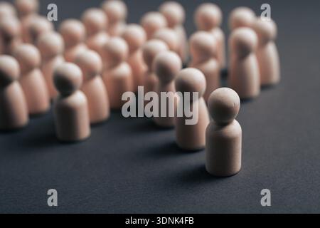 Conceptual image of a single wooden figure separated from a group, symbolizing individuality, leadership, exclusion, isolation, diversity, or standing Stock Photo