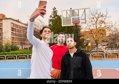 Three friends posing for a selfie on an outdoor basketball court, enjoying leisure time and camaraderie together Stock Photo