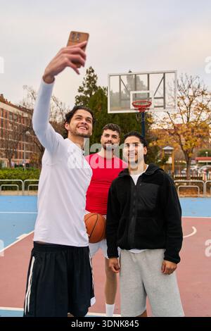 Three young men capturing a moment of friendship and youth on a basketball court, connecting through technology Stock Photo