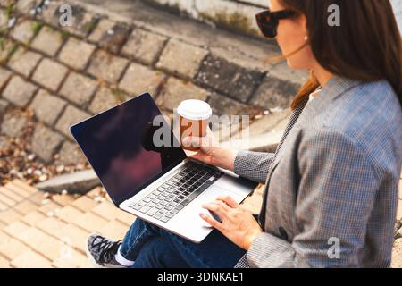 Modern woman using her laptop on steps outdoors in city. Stock Photo