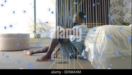 Sitting man leaning against bed in bedroom, in light tee and shorts, phone nearby, digital overlay Stock Photo