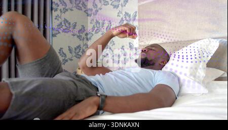 Lying man wearing blue tee gray-shorts raising hand near face on bed in bedroom, with watch Stock Photo