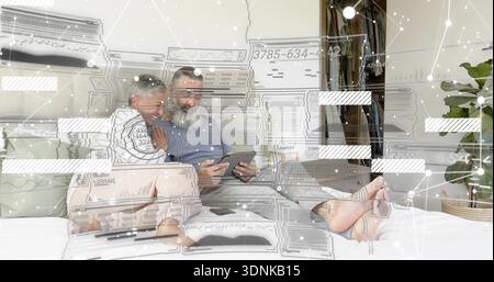Holding tablet, mature couple leaning on bed at home, wearing casual clothes, digital overlay Stock Photo