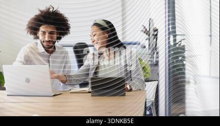 Collaborating coworkers in white shirt and blazer with headband pointing at silver laptop at table Stock Photo
