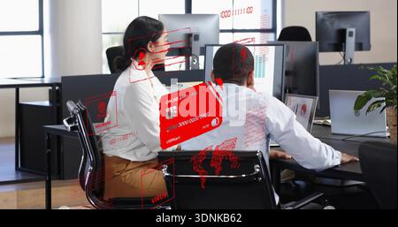 Reviewing two staff in white shirts at screens in open-plan office with red holographic overlays Stock Photo