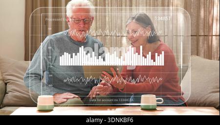 Senior couple examining tablet in living room, viewing translucent digital analytics overlay Stock Photo