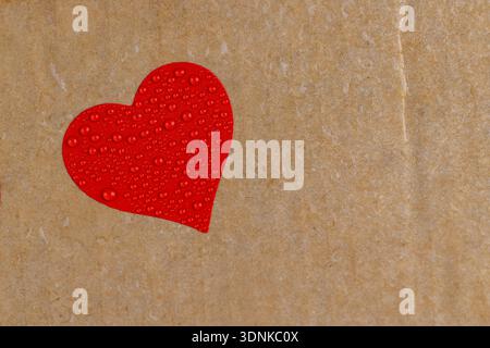 wet hard yellow cardboard for packaging goods and products with red plastic hearts glued on , a piece of corrugated cardboard with one red heart cover Stock Photo