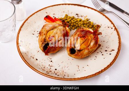Roasted whole quails served on plate with peas and fried carrot Stock Photo