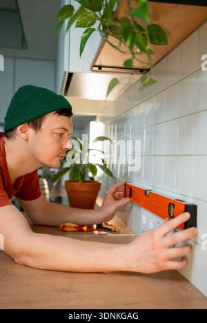 Man using a spirit level inspecting electrical socket installation in a modern kitchen, ensuring horizontal alignment during home improvement and renovation, focusing on detail Stock Photo