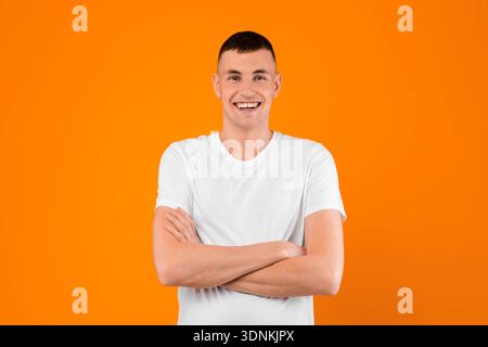Young Man Smiling To Camera Posing Crossing Hands, Yellow Background Stock Photo