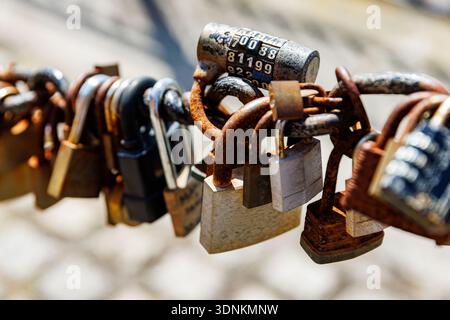 Close view of many rusty padlocks hanging on a metal chain outdoors, symbolising love and memories. Stock Photo