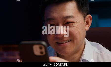 Laughing smiling Asian middle-aged business man scrolling mobile phone Chinese businessman Japanese male employer laugh smile having fun with Stock Photo