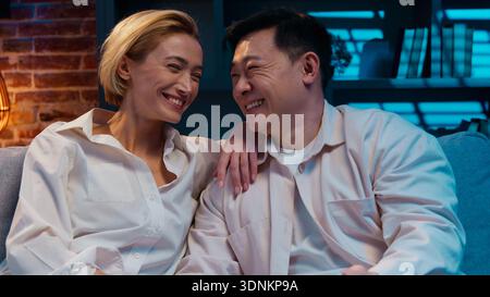 Diversity couple looking at each other smiling toothy happy laughing spending evening at home joyful positive laugh smile Asian man Caucasian woman Stock Photo