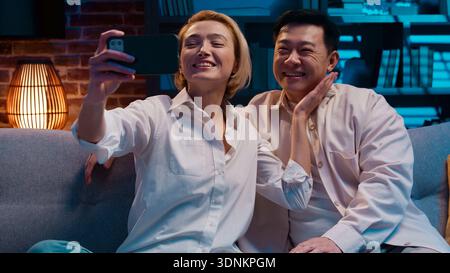 Happy multiracial couple talking video call with mobile phone smiling talk conference married spouses diverse Asian man and Caucasian woman positive Stock Photo