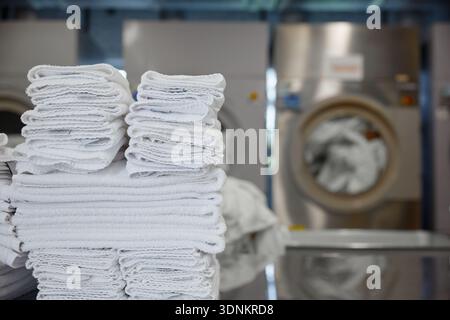 A stack of clean towels is on a table in front of a washing machine Stock Photo