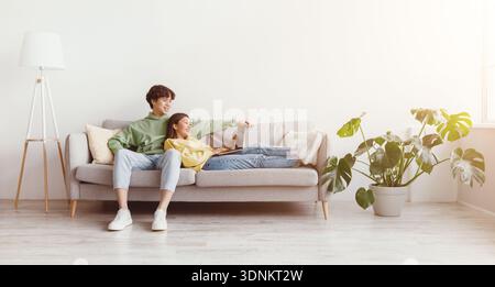 Cheery young Asian couple sitting on sofa, using laptop computer, communicating remotely, having video call at home Stock Photo
