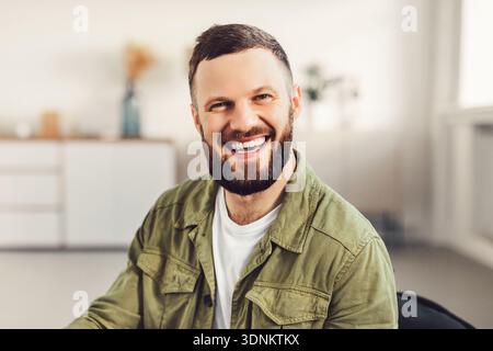 Happy Bearded Guy Smiling Sitting In Chair At Home Stock Photo