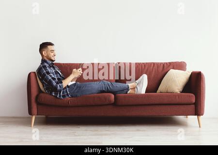 Man Sitting on Red Sofa and Using Smartphone in a Simple Interior Space Stock Photo