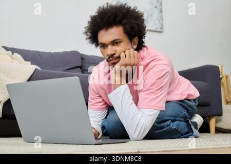 A handsome young man is lying on the floor, focused on his laptop in a cozy space. Stock Photo