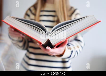 Close-up of woman holding open book toward the camera. Reading, education and knowledge concept with shallow depth of field and copy space. Stock Photo
