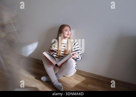 Female reader in striped sweater enjoying literature indoors. Calm home atmosphere, natural light and personal growth concept. Stock Photo