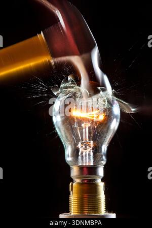 HAMMER KILLS OLD TUNGSTEN LIGHT BULB - SYMBOLISING THE DEMISE OF OLD TECHNOLOGY AND IN WITH NEW. Stock Photo