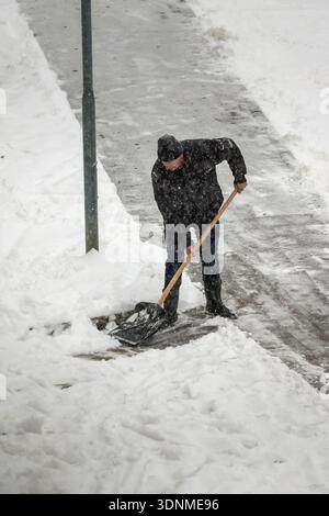 man shoveling snow from pathway in snowfall Stock Photo