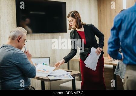 Businesswoman presents documents to colleague during an indoor office meeting with charts and data Stock Photo