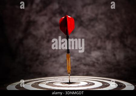 Dart arrow hitting the center of dartboard with red dart arrow Stock Photo