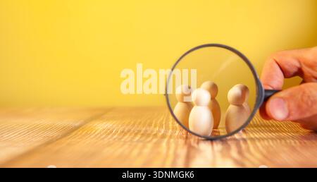 human figure holding magnifying glass in hand on wooden table Stock Photo