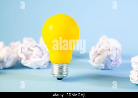 Yellow light bulb with crumpled paper balls on blue background. Stock Photo