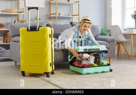 Woman ready for summer vacation happy packing suitcase at home, two luggage wheel bags Stock Photo