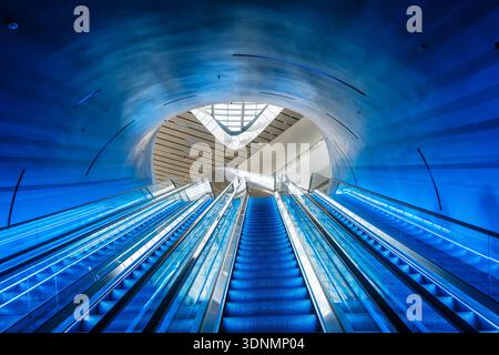 Futuristic blue illuminated escalators in curved modern tunnel with architectural perspective symmetry in Chengdu city, China. Symmetry, minimalism Stock Photo