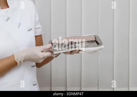 A female podiatrist  pedicurist holding sanitized set tools for working with a client. Light background with copy space Stock Photo