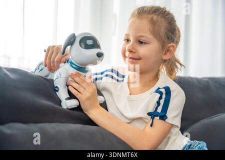 Child interacting with robotic dog while sitting on sofa at home. Artificial intelligence technology and human robot interaction in modern domestic Stock Photo