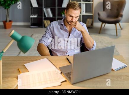 Concerned businessman at laptop analyzing papers and accounting data during audit Stock Photo