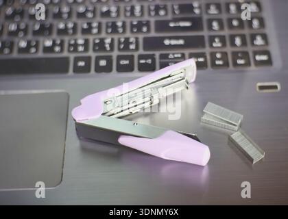 An image of a light purple stapler and staples lying on the surface of a laptop. Stock Photo