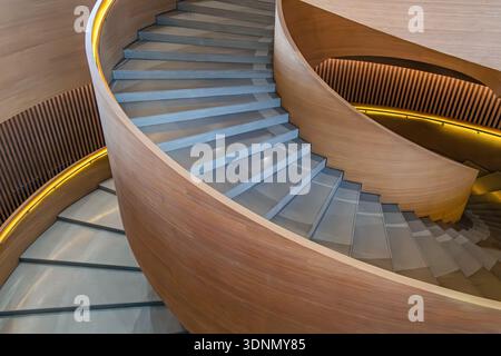 Modern curved wooden spiral staircase with gray concrete steps and minimalist architectural design. Abstract architecture background. Organic and Stock Photo