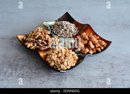 Three types of nuts (walnut, peanut, cashew) and sunflower seeds in a colorful bowl against a grey background Stock Photo