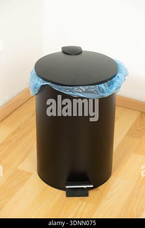 Black Pedal Trash Can with Blue Garbage Bag Indoors. Stock Photo