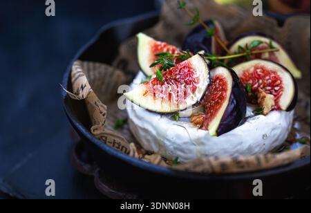 Camembert or brie cheese with fresh figs walnuts  and honey on iron frying pan, over dark background Stock Photo